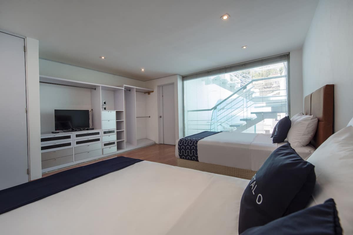 A bedroom with a bed, a TV, a wardrobe, and a window with a view of a staircase.