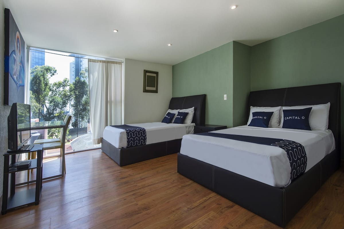 A hotel room with two beds, a desk, and a view of the city.