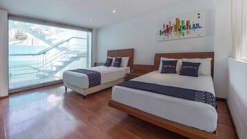 A modern hotel room with two beds, a large window with blinds, a staircase outside, and a cityscape painting on the wall.