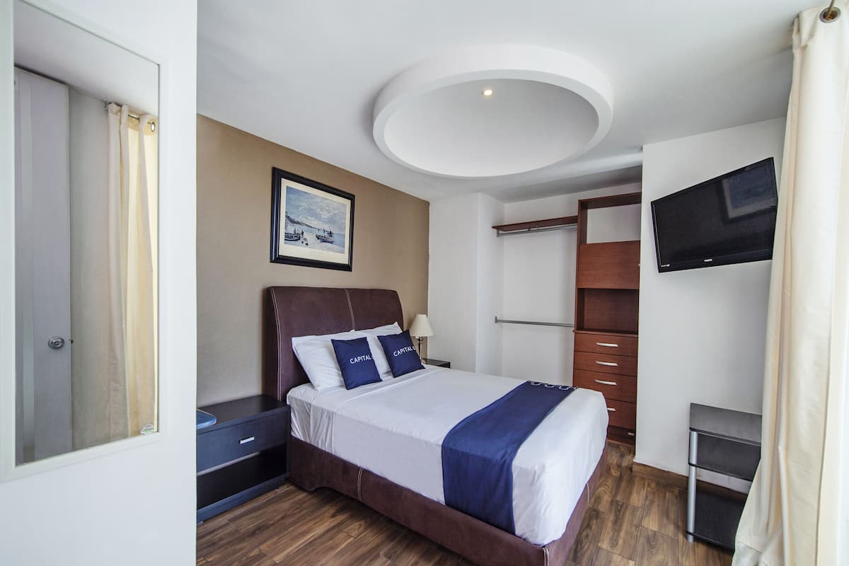 A hotel room with a bed, a nightstand, a TV, a wardrobe, and a ceiling light.