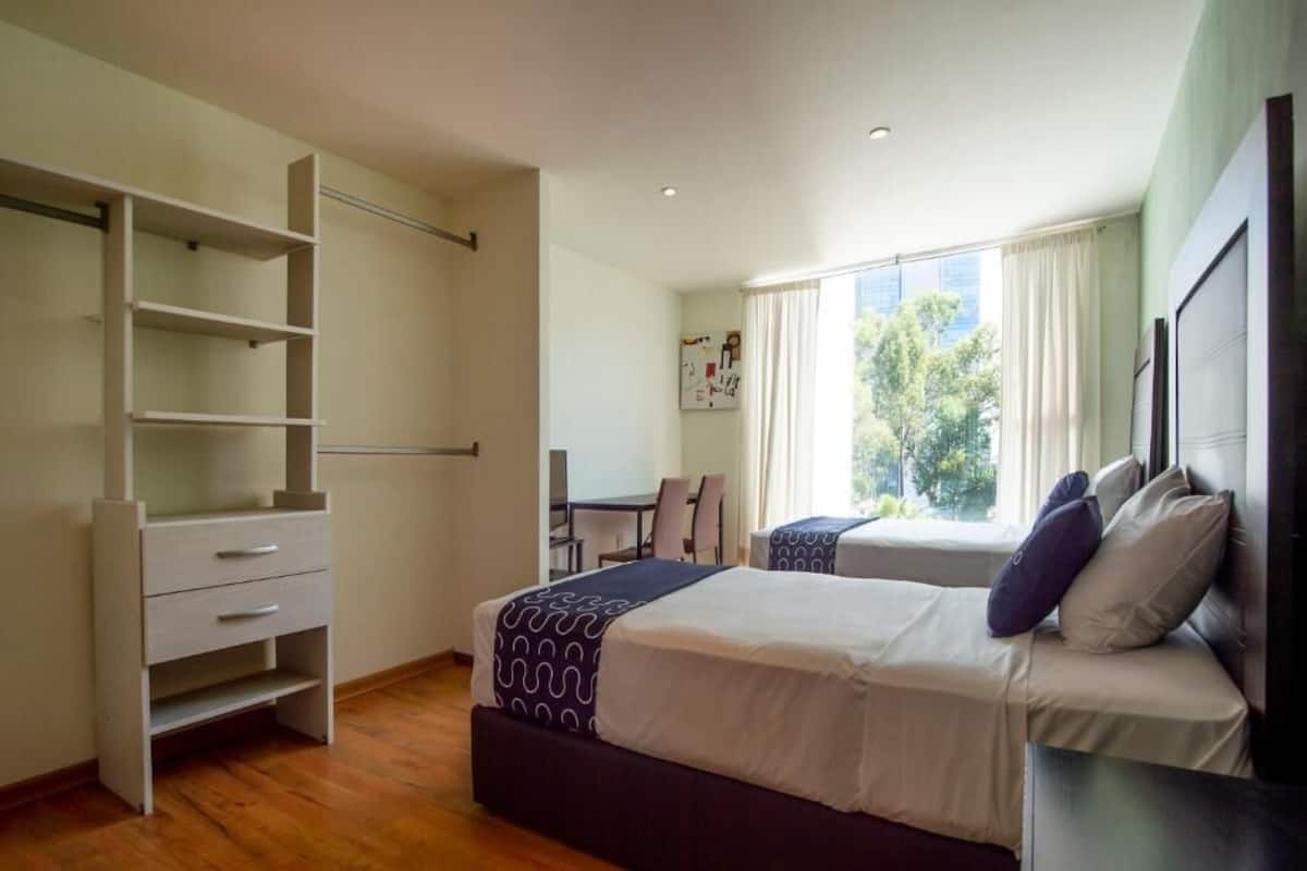 A bedroom with a bed, a wardrobe, a desk, and a window with a view of trees.