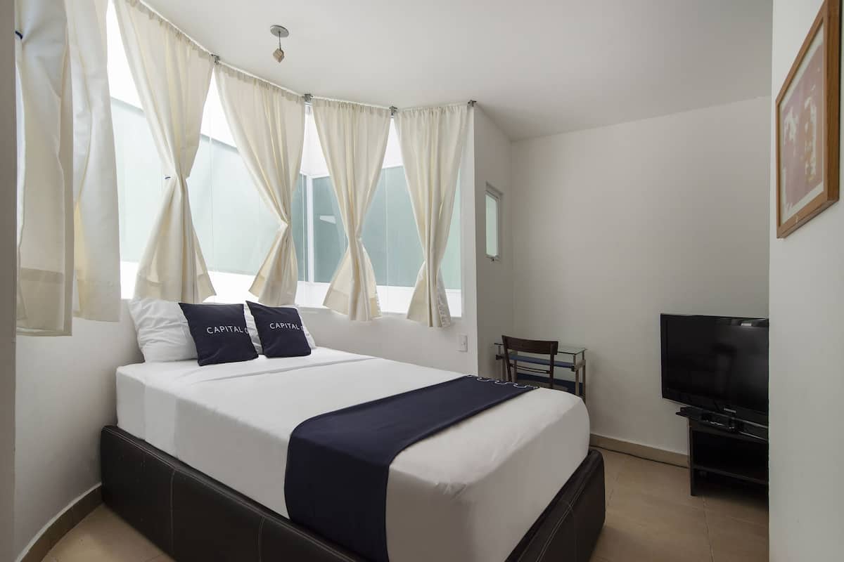 A hotel room with a bed, a TV, and a desk.