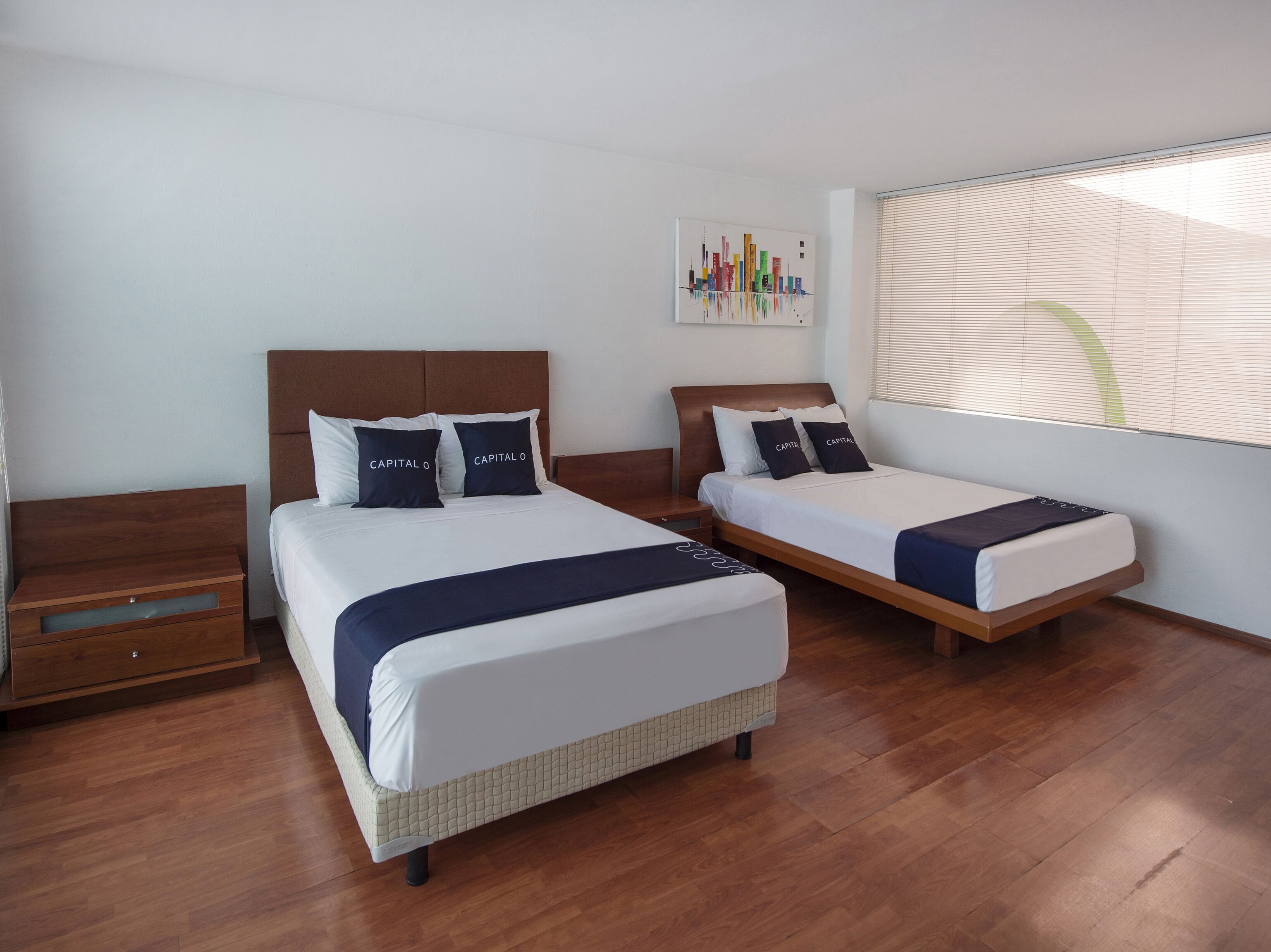 Habitación de hotel con dos camas, piso de madera, una mesita de noche, un cajón y una ventana con persianas.