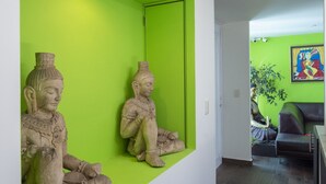 Un pasillo con una pared verde decorativa, dos estatuas sentadas, un sofá y un cuadro.