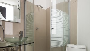 Un baño moderno con cabina de ducha de vidrio, lavamanos de vidrio y inodoro blanco.