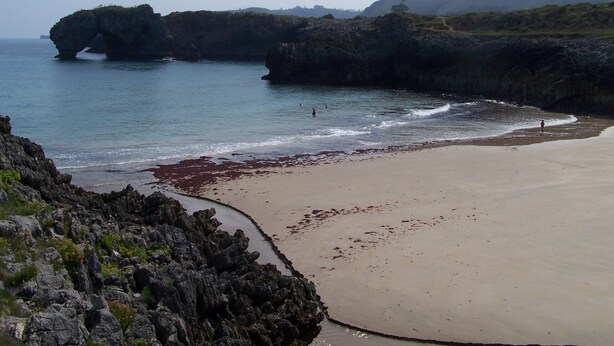 A coastal landscape with a sandy beach, rocky cliffs, and calm sea.