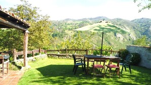 A patio with a table and chairs, surrounded by a wooden fence and a stone wall, overlooking a hilly landscape.