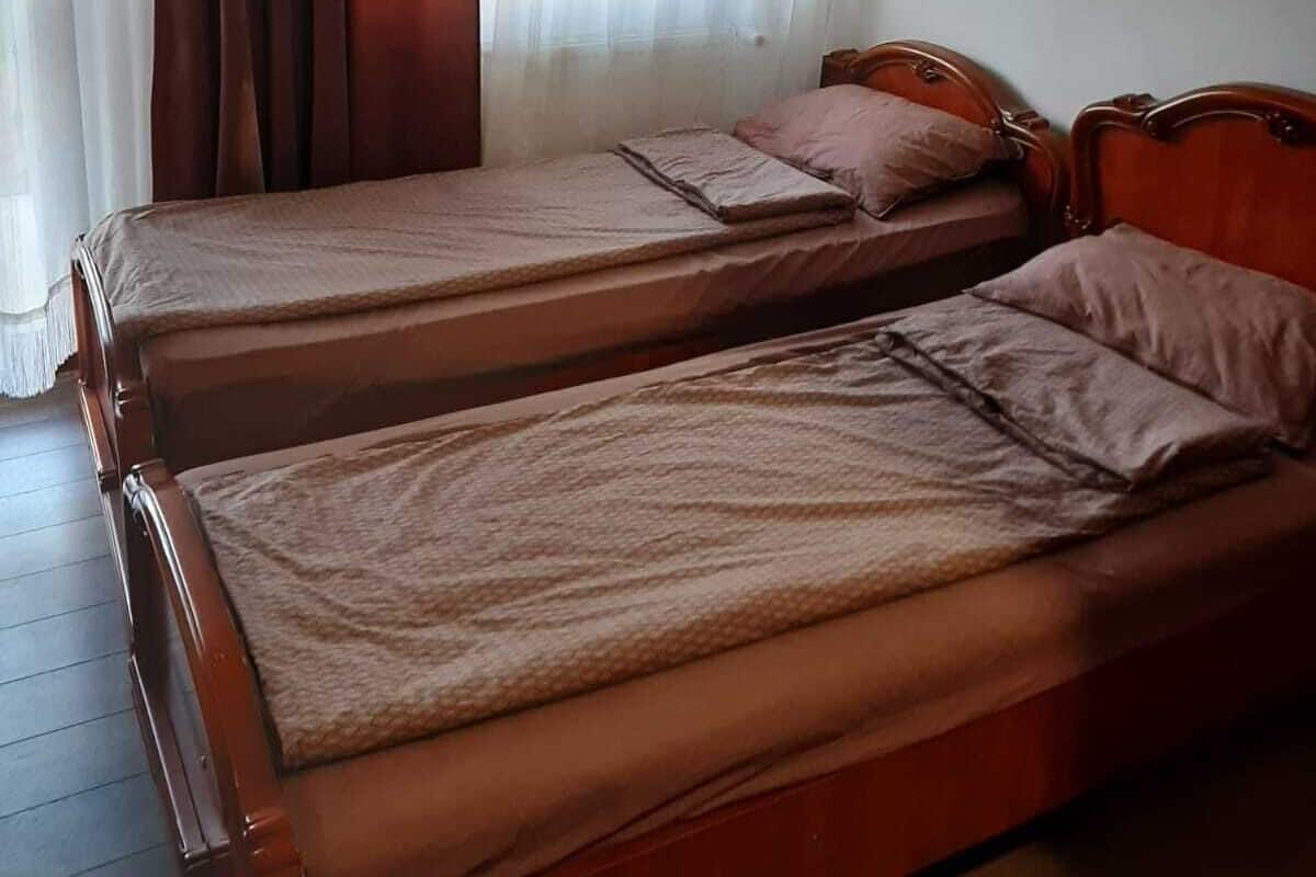 Ein Zimmer mit zwei Holzbetten, einem Fenster mit durchscheinenden weißen Vorhängen und einer schrägen Decke.