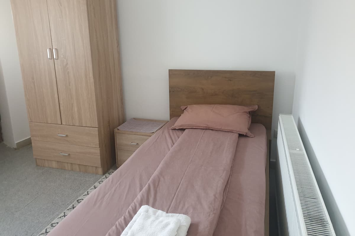 Ein Schlafzimmer mit einem Einzelbett, einem Holzschrank, einem Nachttisch und einer Heizung.