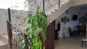 Una escalera con barandilla de metal, una planta en maceta y un comedor con sillas y una mesa.