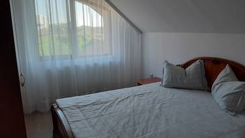 Un dormitorio con cama, mesita de noche y ventana con cortinas translúcidas.