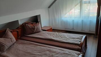 Una habitación con dos camas, una mesita de noche y una ventana con cortinas translúcidas.