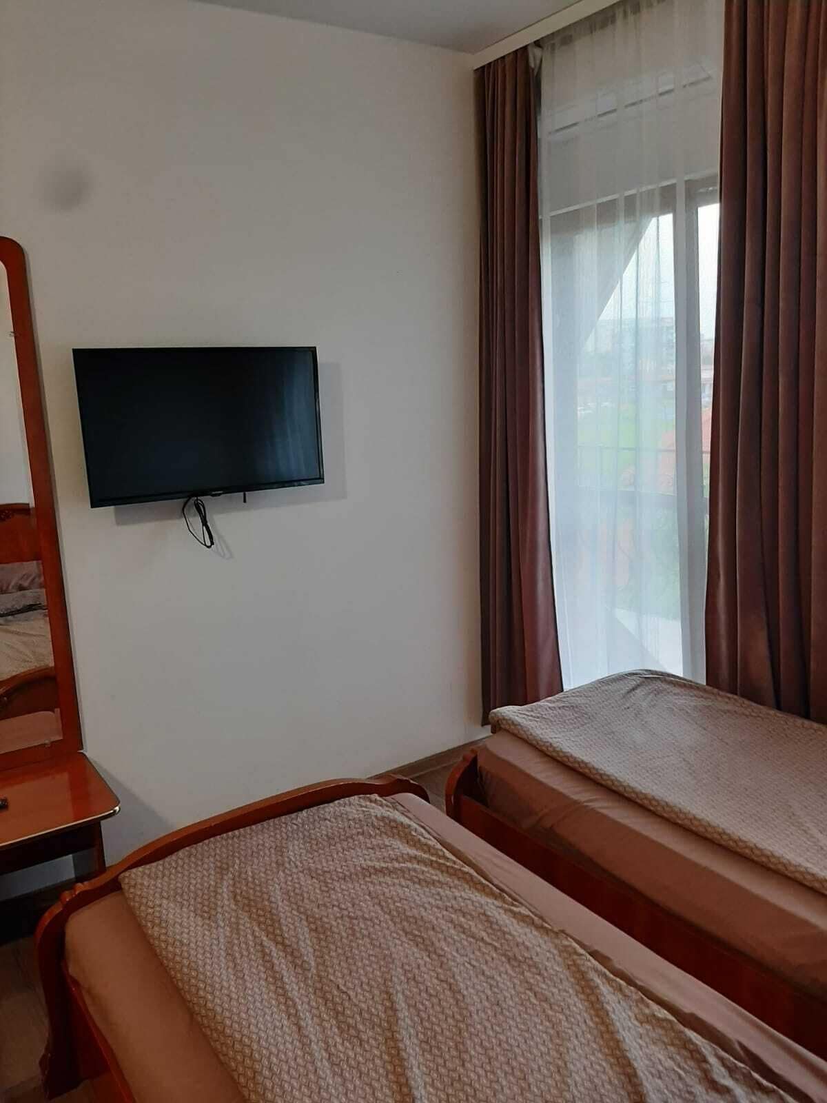 A room with a bed, a TV mounted on the wall, and a window with curtains.