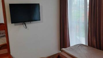 A room with a bed, a TV mounted on the wall, and a window with curtains.