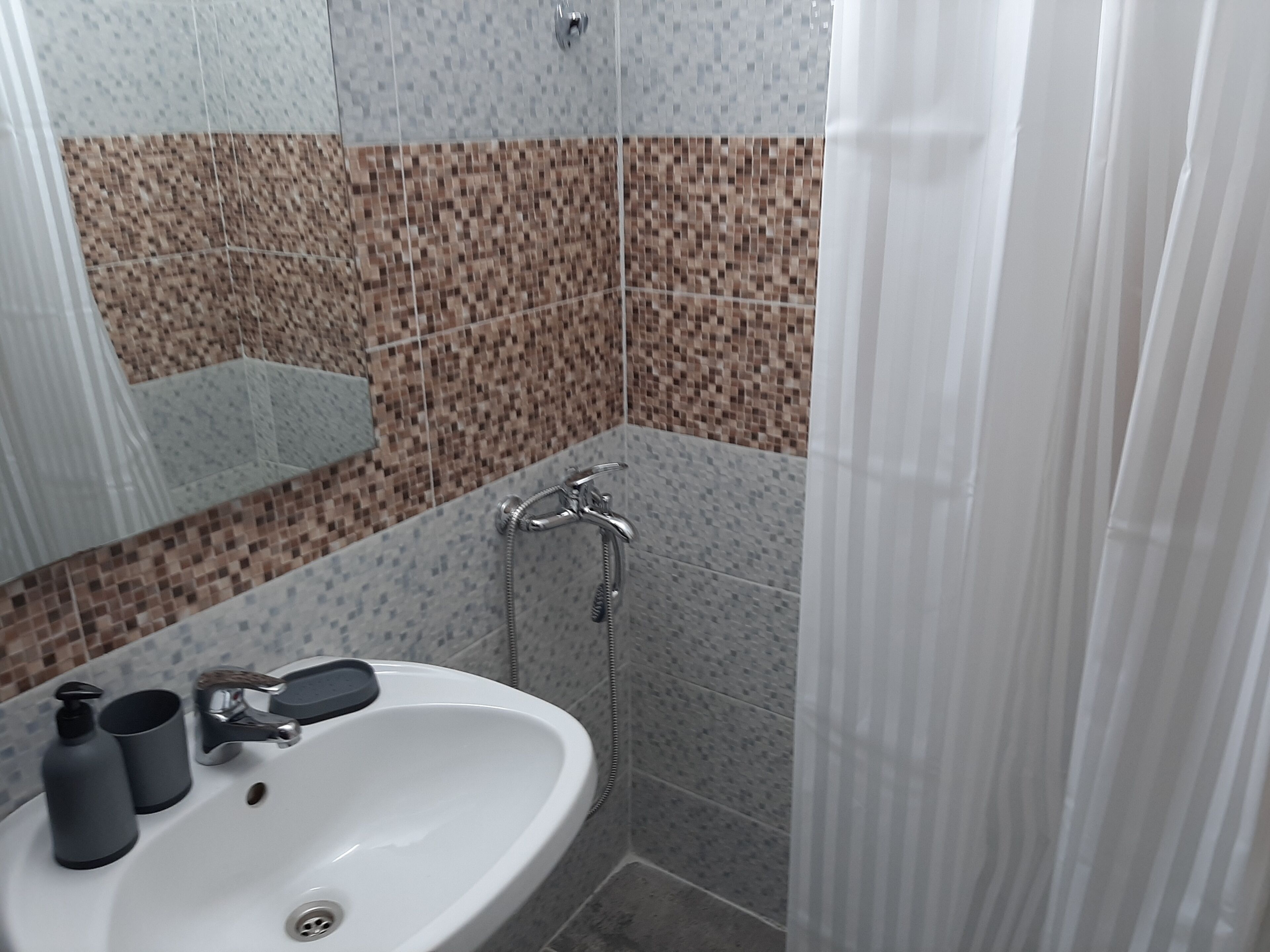 A bathroom with a white sink, a mirror, a shower with a handheld showerhead, and tiled walls.