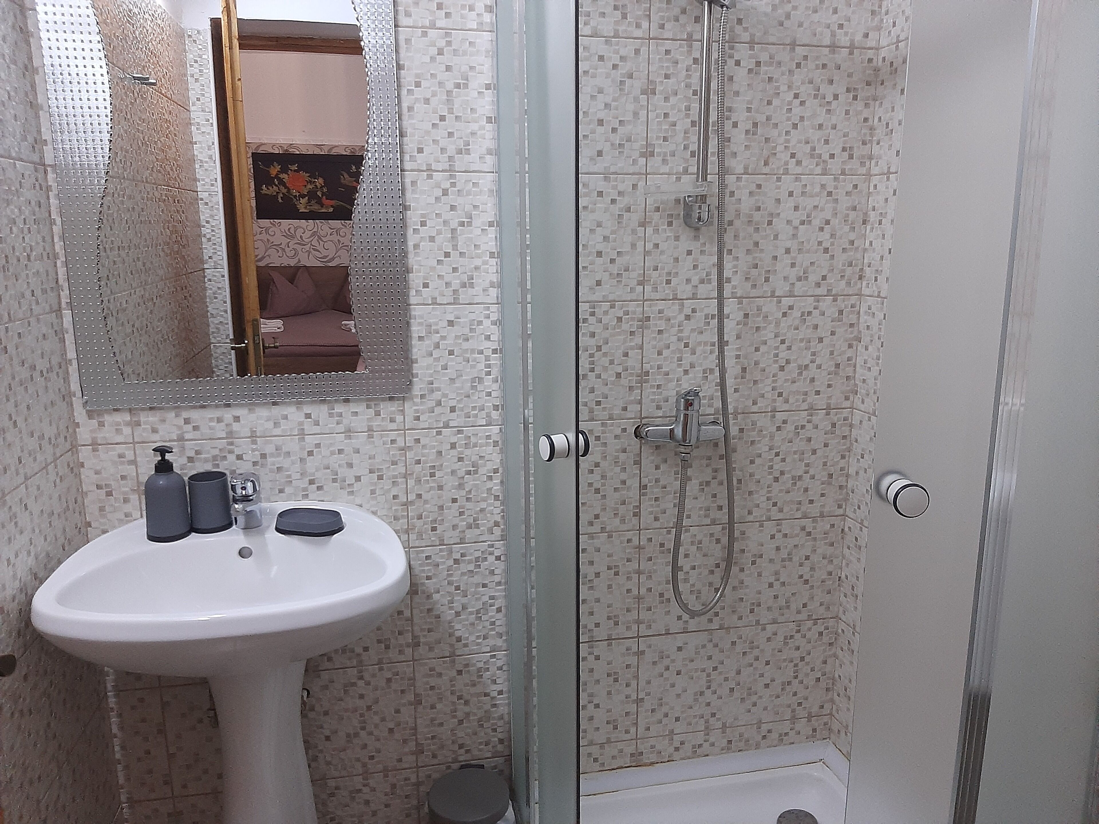 Un baño con lavamanos blanco, un espejo y zona de ducha.