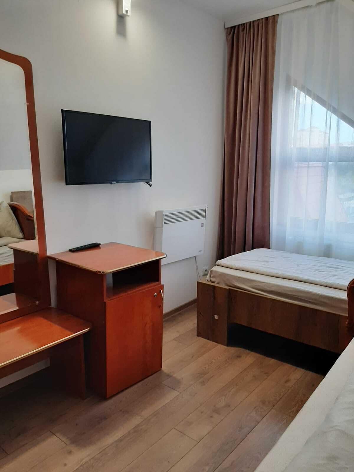 Habitación de hotel con cama, escritorio, silla, televisión y ventana con cortinas.