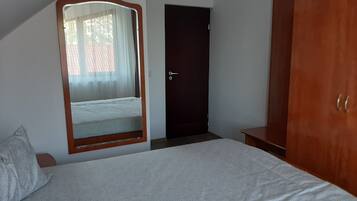 A bedroom with a bed, a wardrobe, a door, and a mirror reflecting a window with curtains.