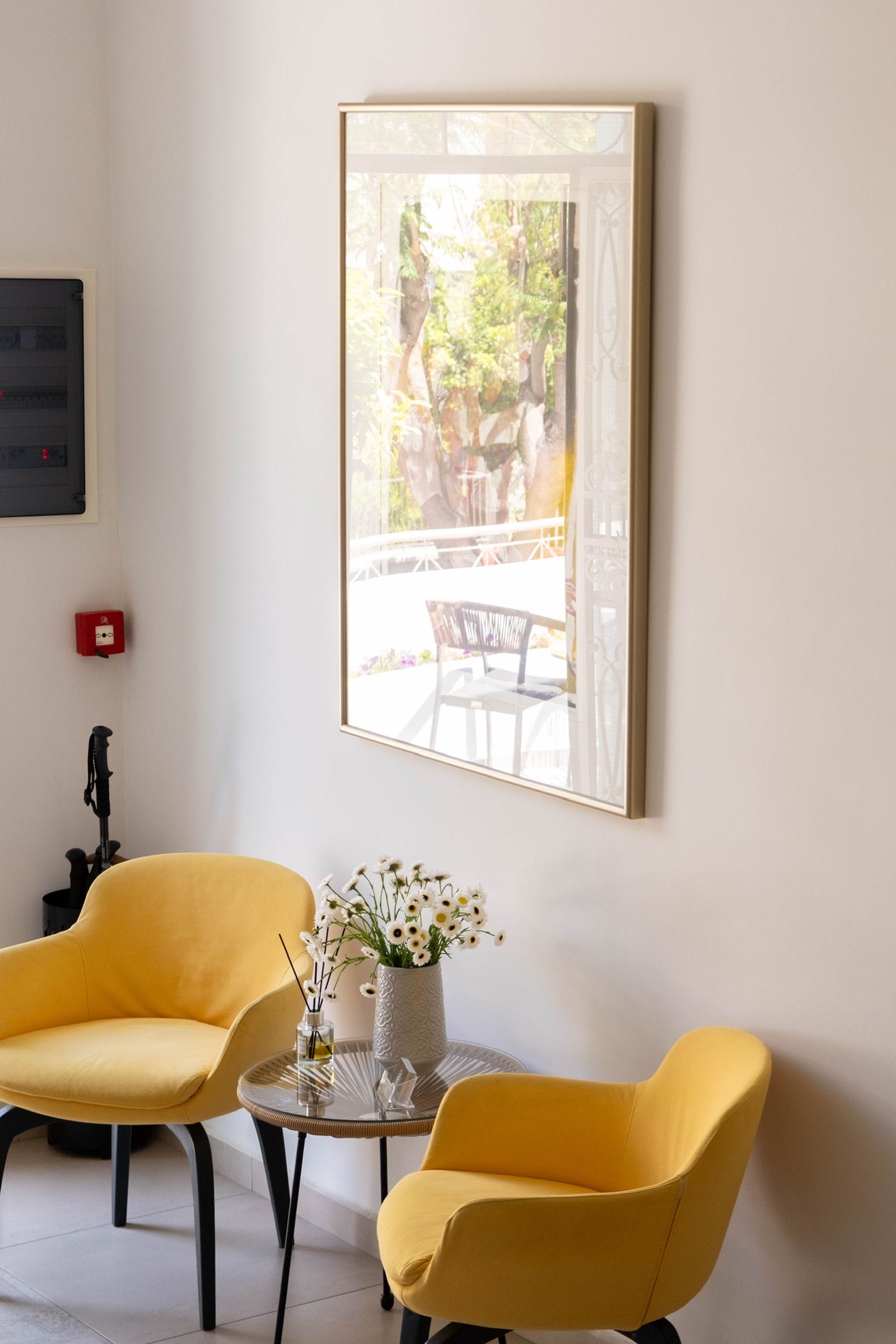A room with two yellow chairs, a small table with a vase of flowers, and a framed picture on the wall.