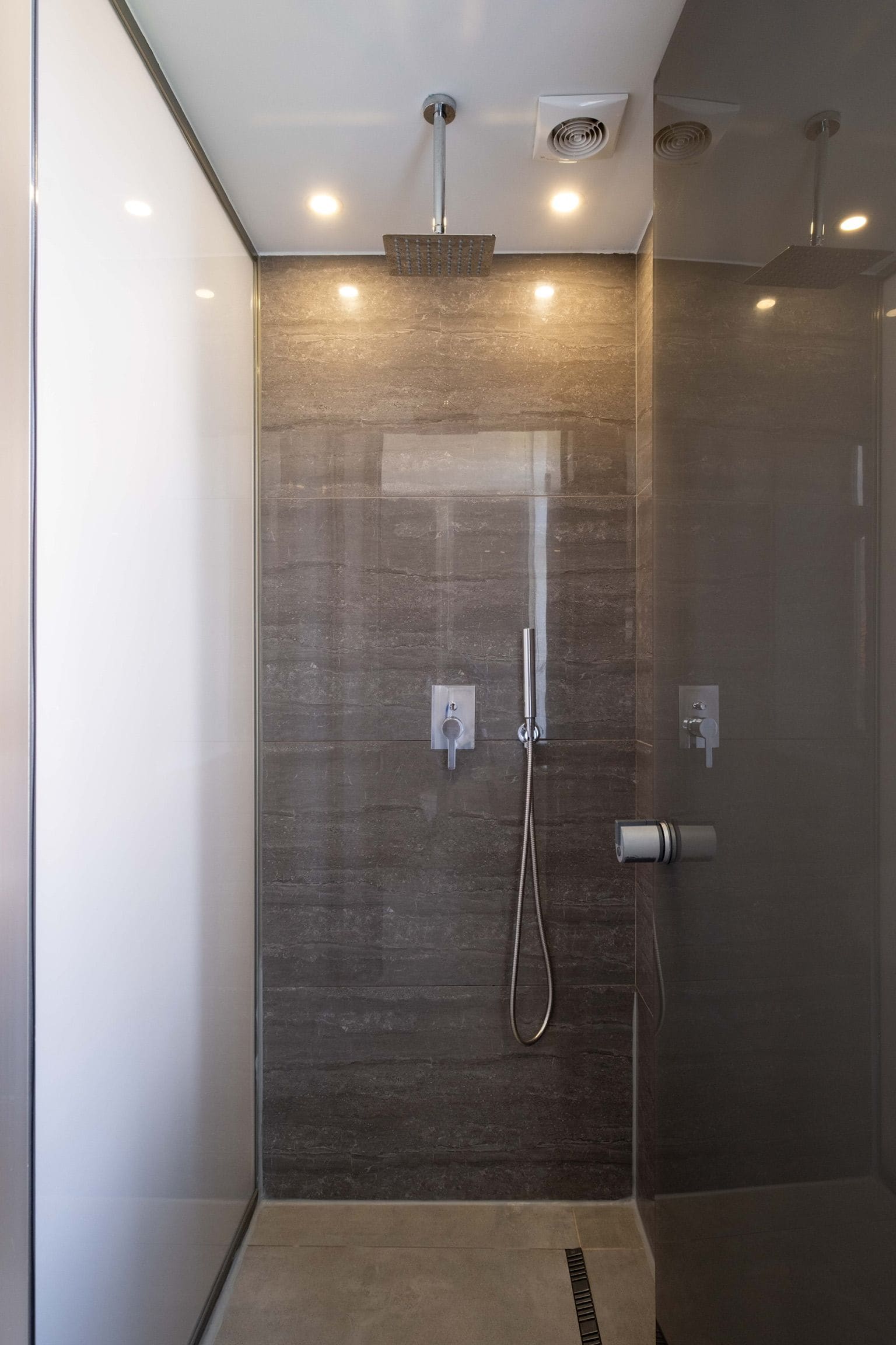 A modern shower with a glass door, a handheld showerhead, and a wall-mounted control panel.