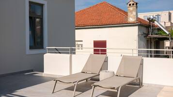 A rooftop terrace with two lounge chairs and a red shuttered window.