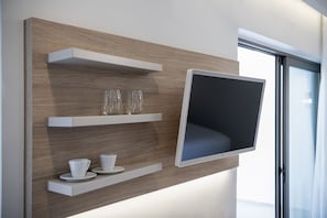 A wall-mounted TV with three shelves below, each holding a cup and saucer. - Epavli Boutique Luxury Suites (Chania)