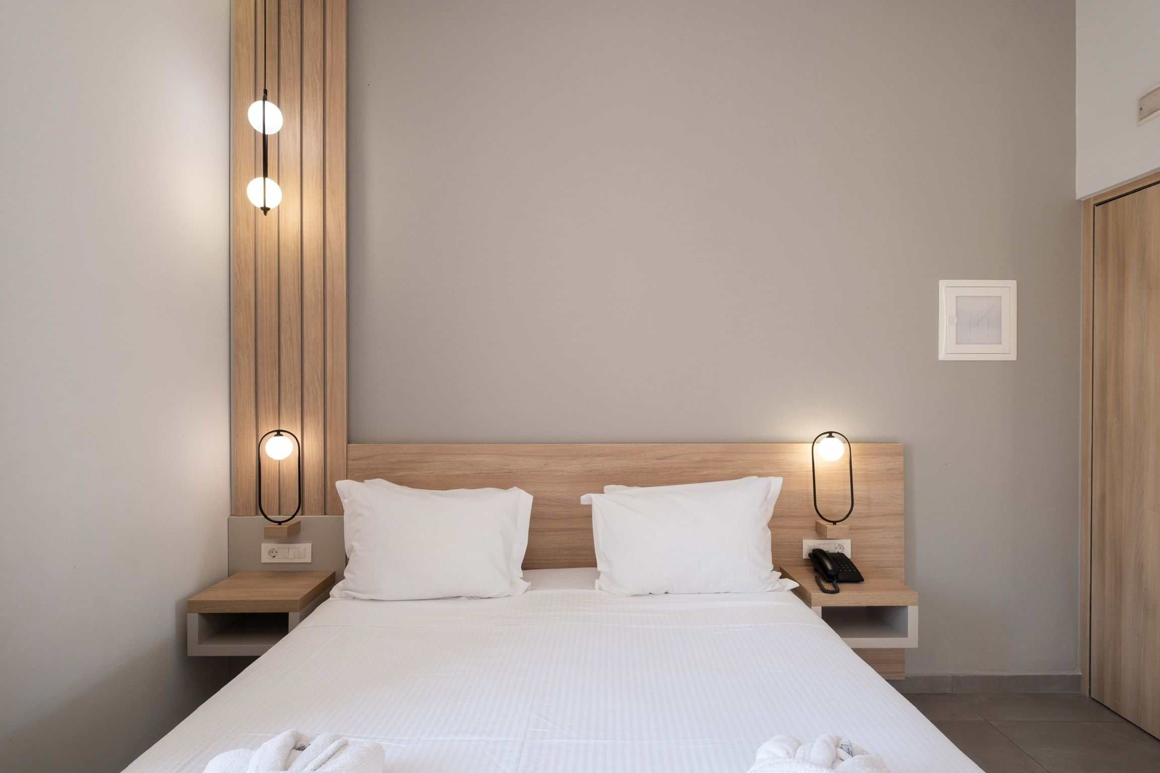 A hotel room with a large bed, two bedside tables, a wooden headboard, and wall-mounted lights.
