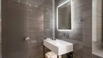 Une salle de bain moderne avec un grand miroir, un lavabo blanc et une douche à parois de verre.