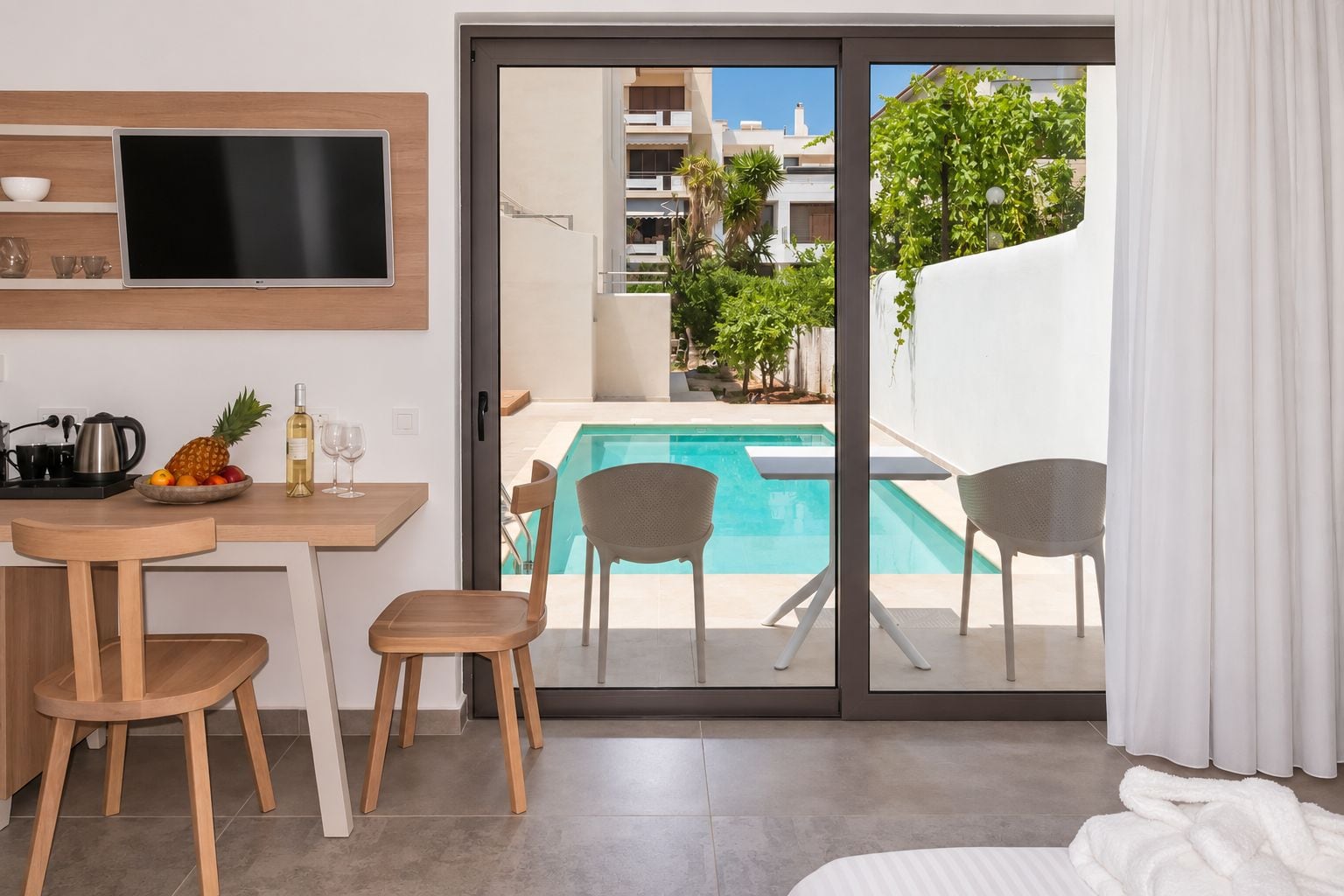 Habitación de hotel moderna con vista a la piscina, un área de comedor con mesa y sillas, y un televisor de pantalla plana en la pared.