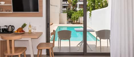 Habitación de hotel moderna con vista a la piscina, un área de comedor con mesa y sillas, y un televisor de pantalla plana en la pared.