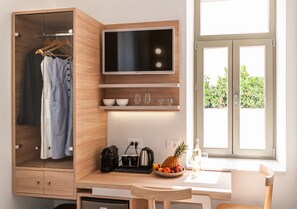 Une chambre moderne dotée d’une armoire en bois, d’un téléviseur à écran plat, d’un coin repas avec une table et des chaises, et d’une fenêtre donnant sur un paysage verdoyant.