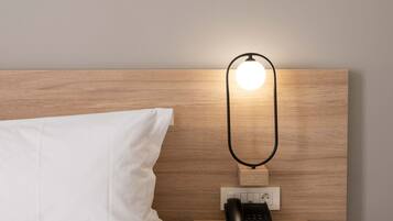 Un lit bien fait, avec du linge de lit blanc, une table de chevet sur laquelle se trouve un téléphone noir et un luminaire fixé au mur.