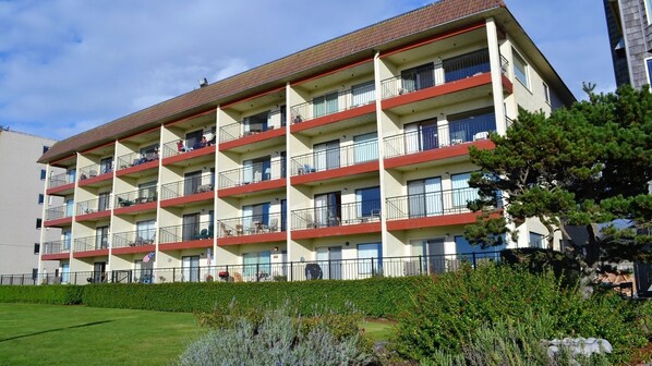 Een hotel met meerdere verdiepingen, balkons, een plat dak en een goed onderhouden tuin.