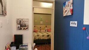Ein Zimmer mit einem Bett, einem Schreibtisch mit Computer und einem Stuhl. An den Wänden sind Dekorationen und ein Schild mit der Aufschrift 'Find the Beauty Around'.