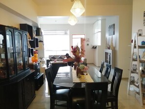 A dining area with a long table, black chairs, and a decorative centerpiece. There is a black cabinet with glass doors on the left, and a white shelf with various items on the right. - Munay Aparthotel (Cusco)