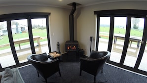A cozy room with a fireplace, two chairs, and large windows offering a view of a deck and outdoor area. - Full holiday home to yourself, up to 21 guests (Atiamuri)
