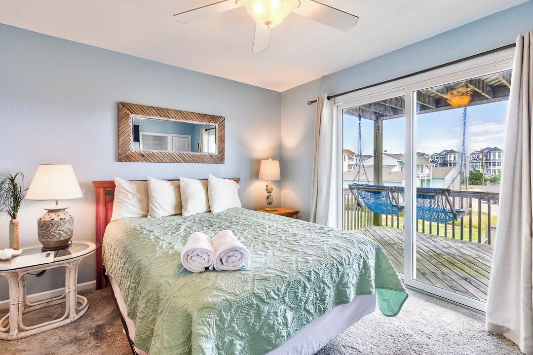 A hotel room with a bed, two bedside lamps, a mirror, and a balcony with chairs.