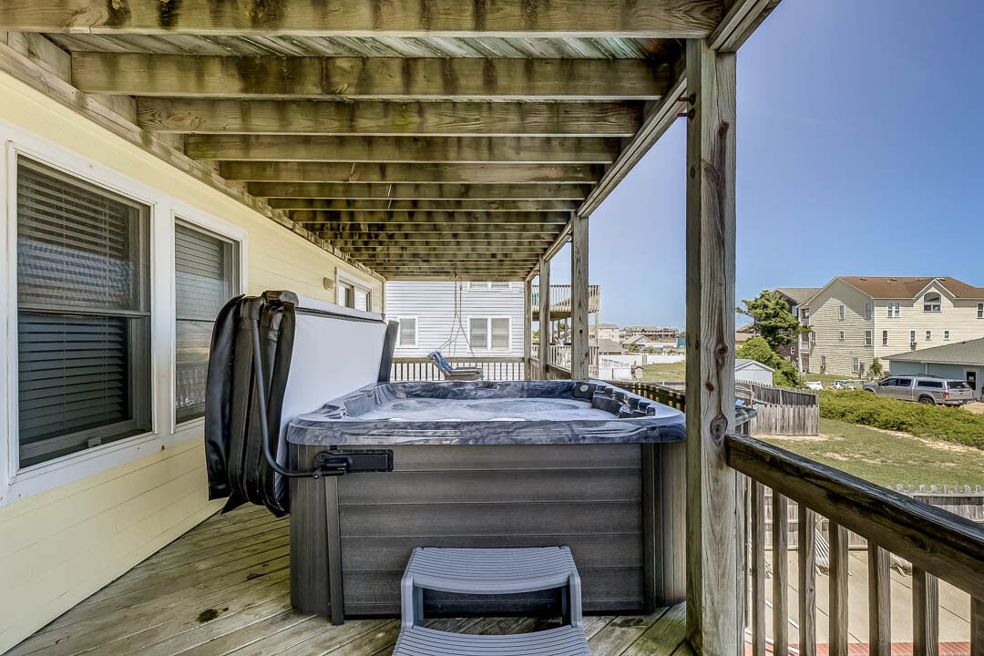 A wooden deck with a hot tub, a covered area, and a view of neighboring houses.