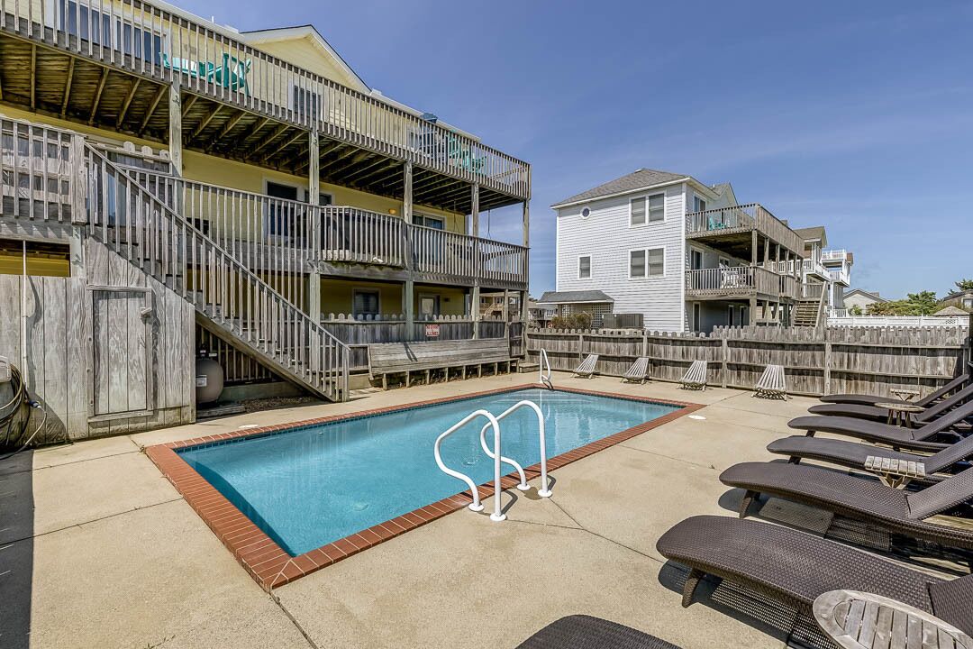 A swimming pool with a wooden deck, lounge chairs, and a wooden fence.