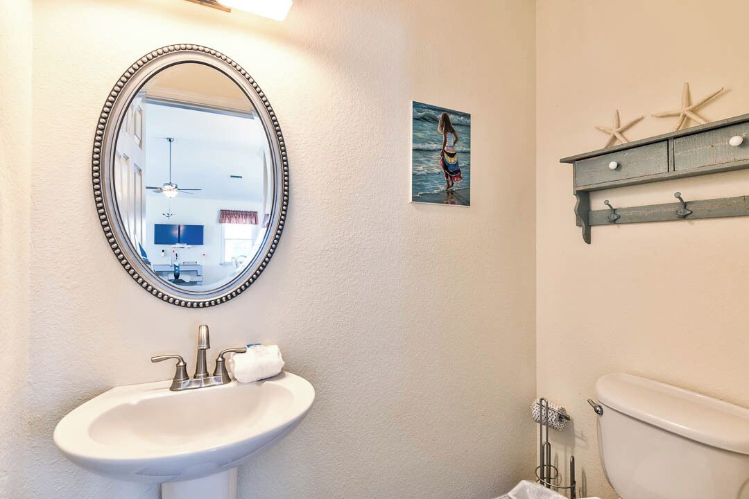 A bathroom with a white sink, a mirror, a toilet, and a small shelf with starfish decorations.