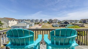 A deck with two turquoise Adirondack chairs, overlooking a residential area with houses and a clear sky. - Sea the Day | 717 ft from the beach | Private Pool, Hot Tub | Nags Head (Nags Head)