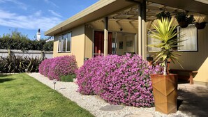 Una casa moderna con porche cubierto, ventanas amplias y un jardín con flores moradas.
