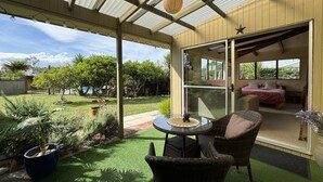 Un patio techado con una mesa y sillas, vista al jardín trasero, y un puerta corrediza que da a un dormitorio.