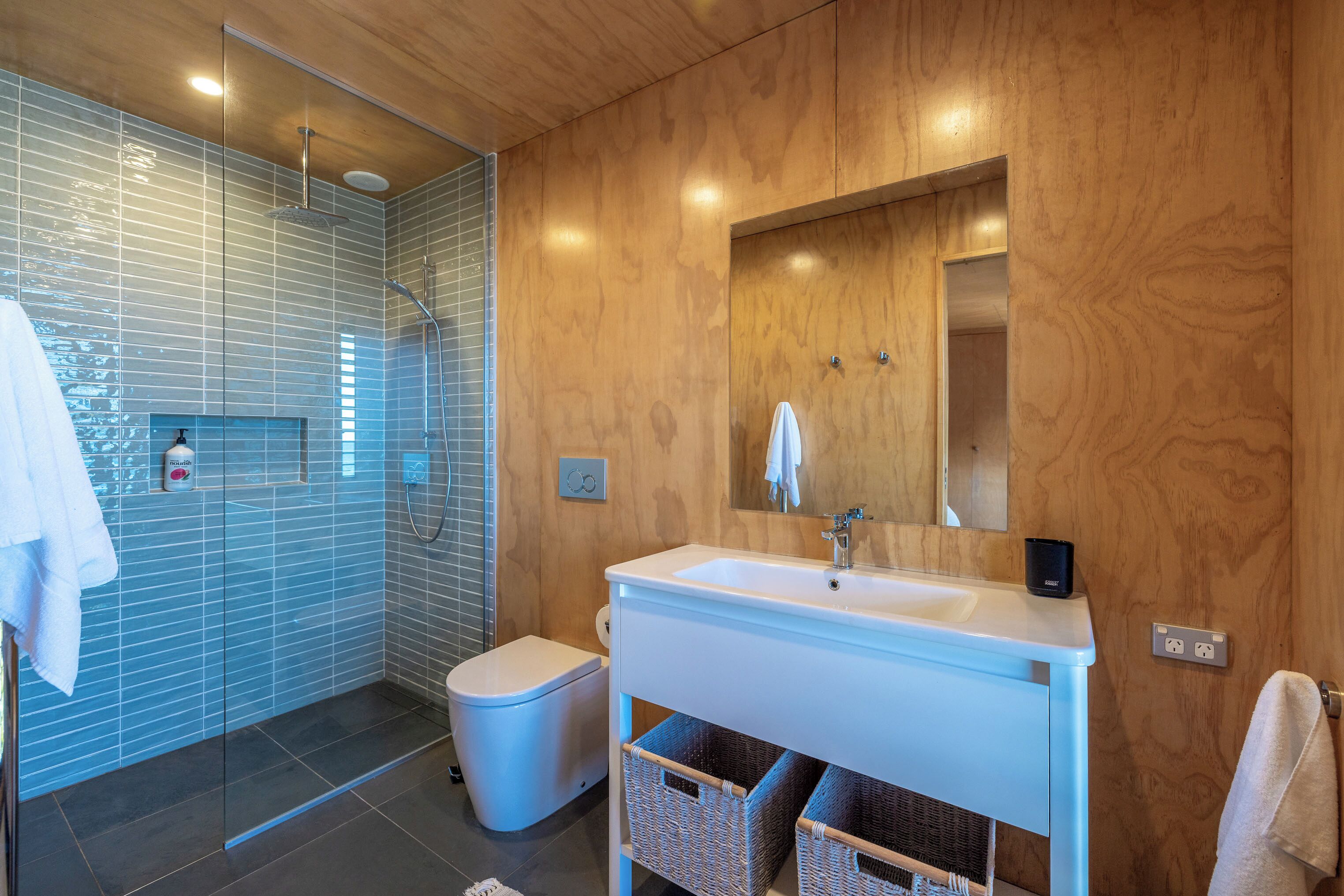 A modern bathroom with a glass shower enclosure, a white sink, and a wooden vanity.