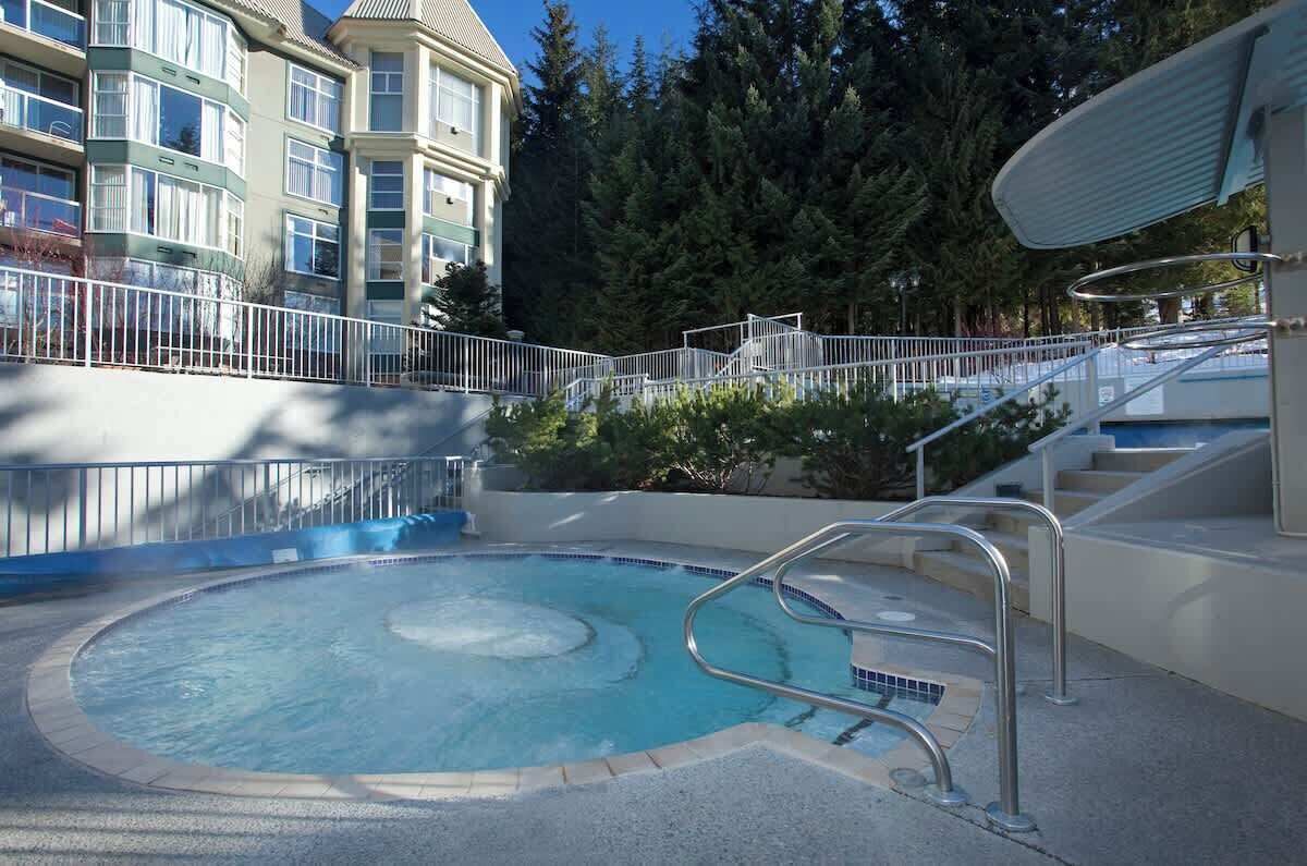 Un espace piscine avec un jacuzzi circulaire, un escalier et un bâtiment doté de nombreuses fenêtres en arrière-plan.
