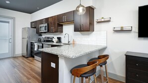 A modern kitchen with dark wooden cabinets, stainless steel appliances, a granite countertop, and a pendant light. - Studio King Suite w/ Kitchen | 201 (Asheville)