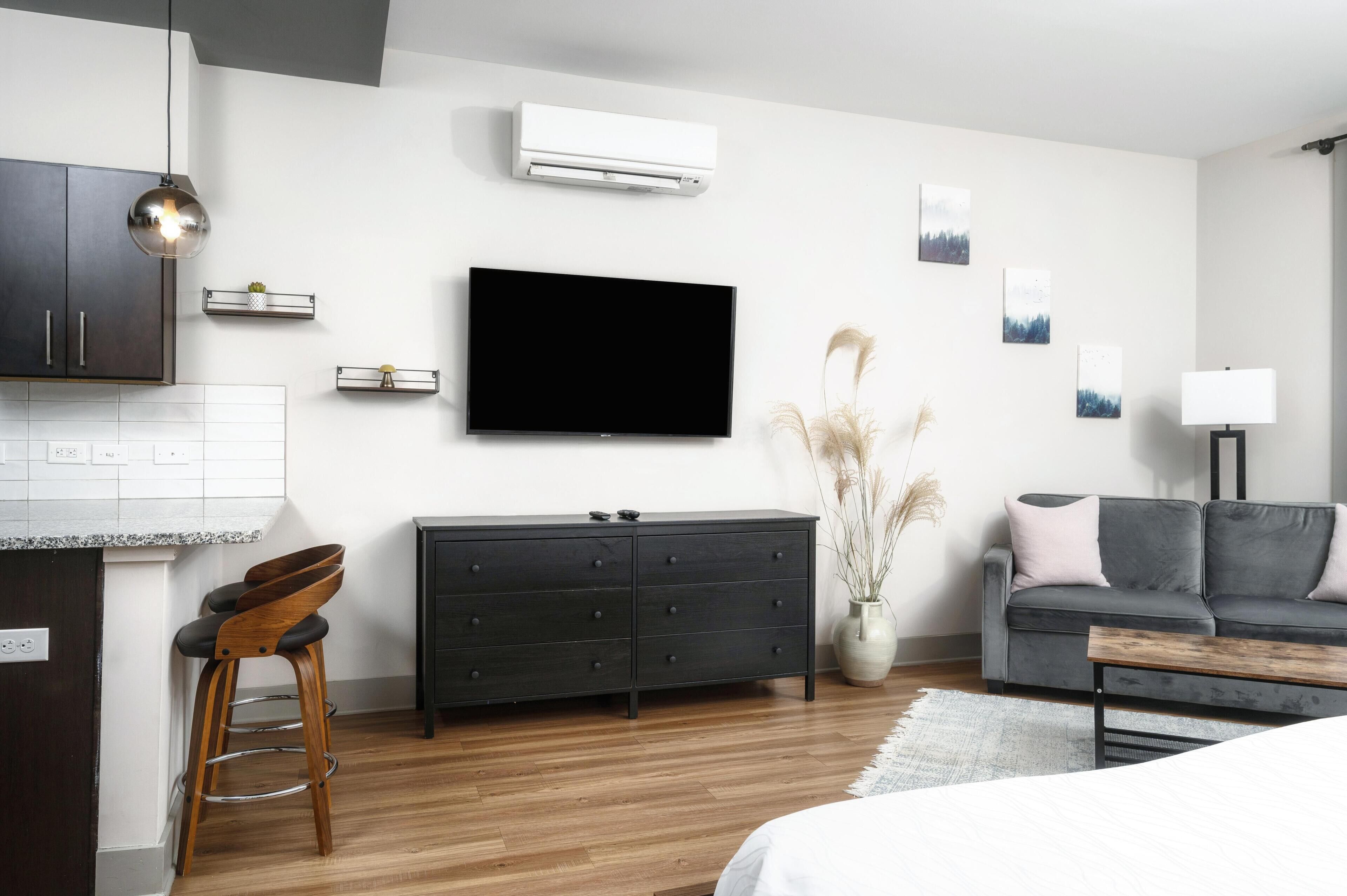 A modern living room with a flat-screen TV, dark wooden furniture, a grey sofa, and a white lamp.