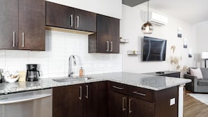 A modern kitchen with dark wooden cabinets, a granite countertop, and a built-in dishwasher. - Studio King Suite w/ Kitchen | 201 (Asheville)