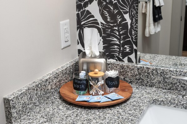 Un mostrador de baño con encimera de granito, un dispensador de pañuelos, un portalápices para cepillos de dientes y una taza etiquetada 