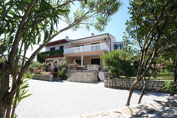 A two-story building with a balcony, stone walls, and a paved courtyard.